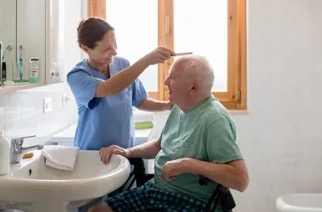 Caregiver gently combing an elderly man’s hair at the bathroom sink