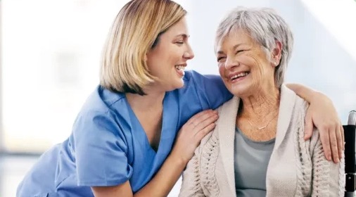 Smiling caregiver in blue scrubs hugging an elderly woman