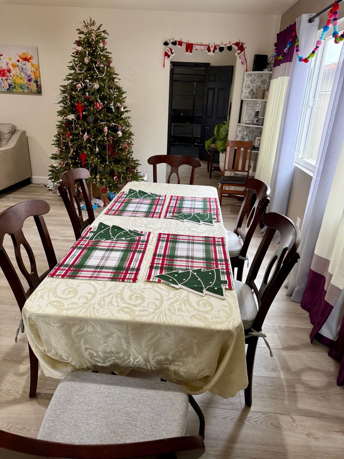 Dining table set with holiday placemats beside a decorated Christmas tree