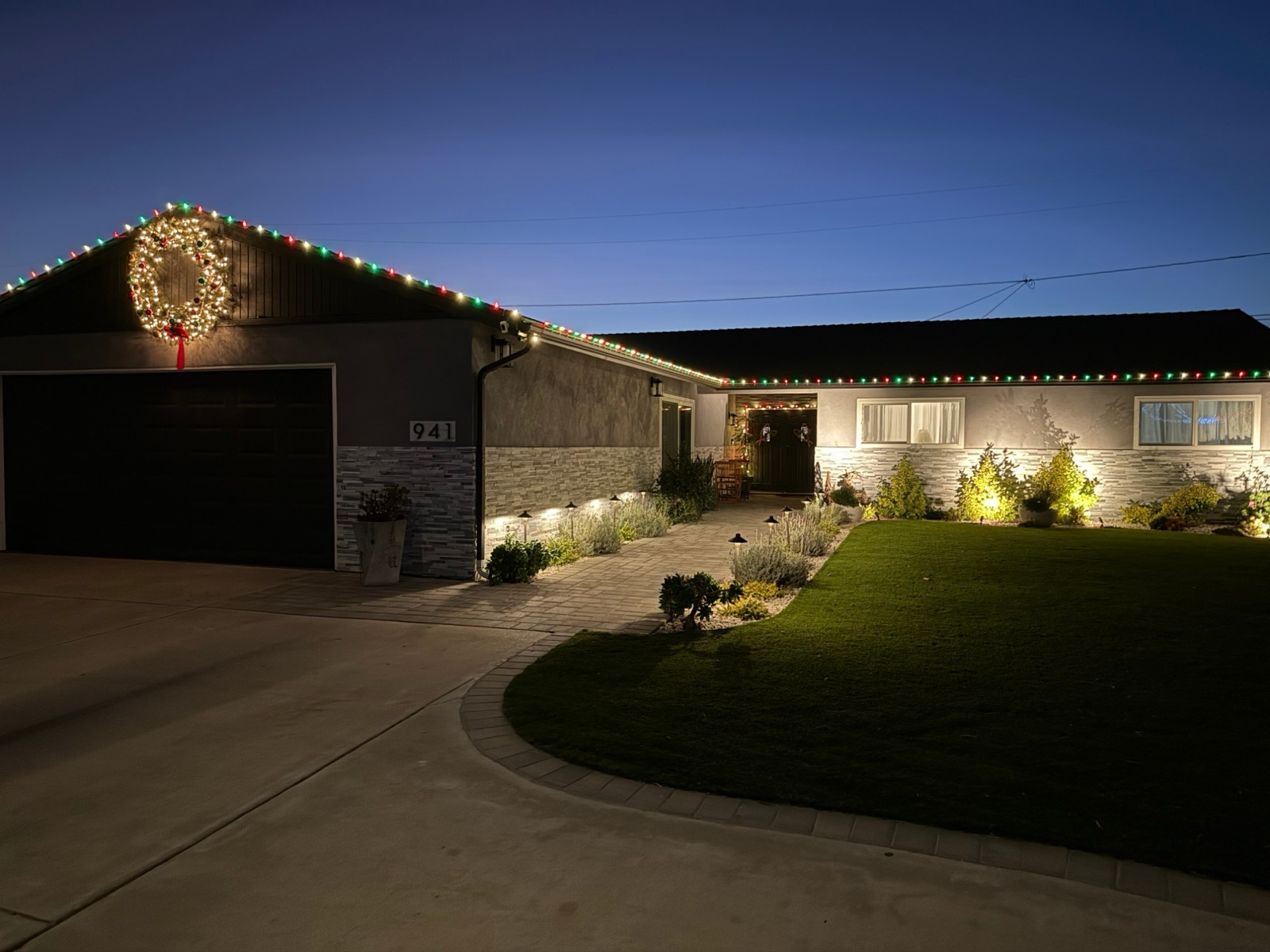 Front of the home at dusk, decorated with holiday lights and a lit wreath