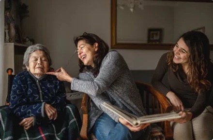 Family members laughing with an elderly woman as they share a photo album
